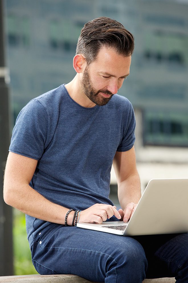 Man researching training programs on a laptop outdoors