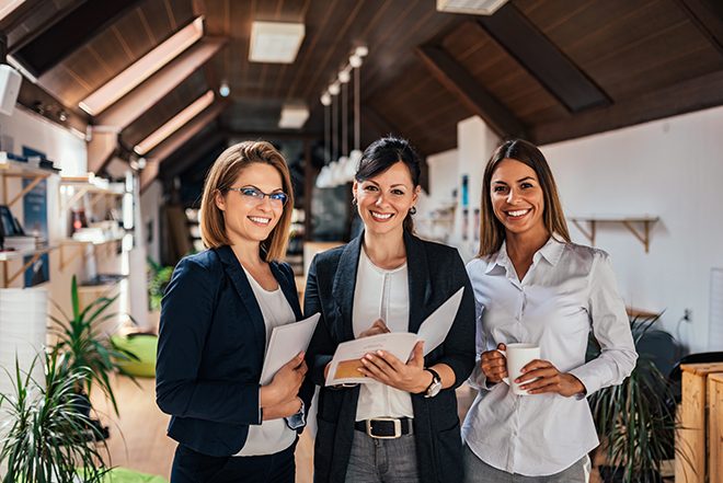 Three women colleagues smiling together in an office